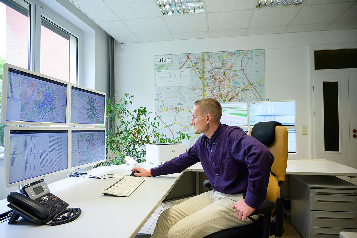 A man at a desk looks intently at his monitors, on which various city maps of Erfurt are open