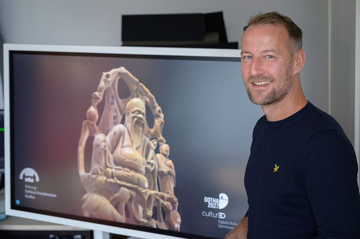 A man standing in front of a monitor looks at the camera with a friendly smile