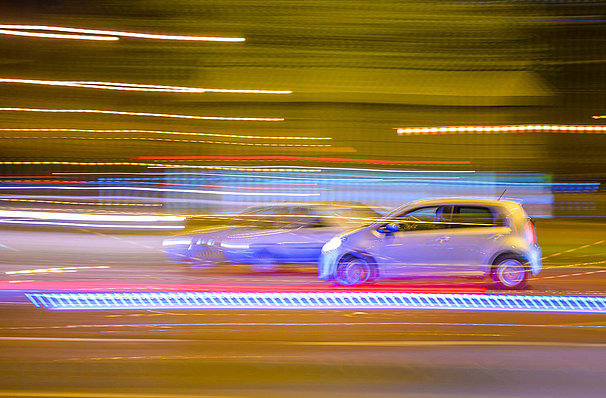  Two cars driving by at night. Cars and lights are blurry because of the speed.